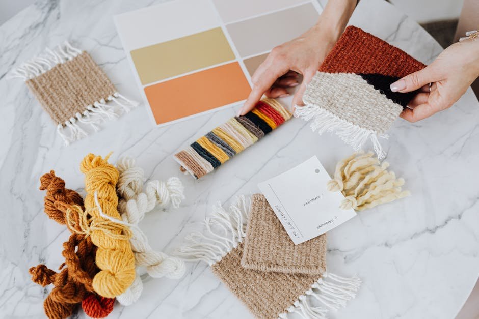 A top view of hands organizing textile samples with yarns and color palette on a marble surface.